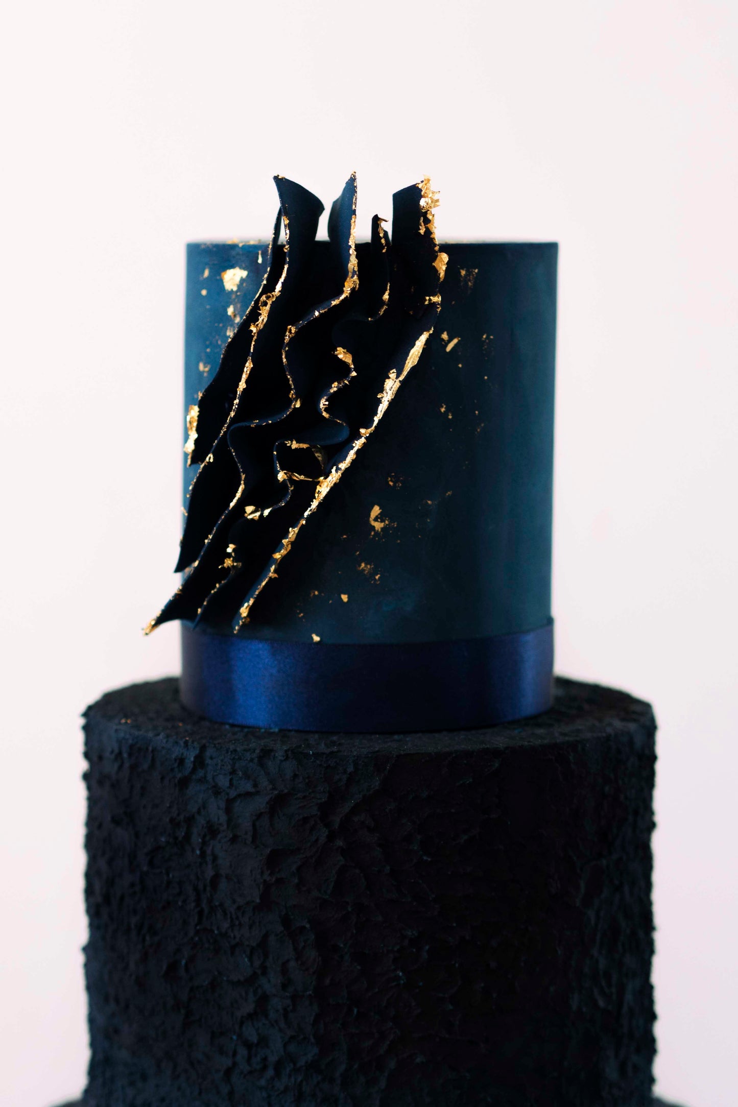 Deep tiered navy blue wedding cake. Middle tier has rough textured icing, top tier is smooth with edible voile