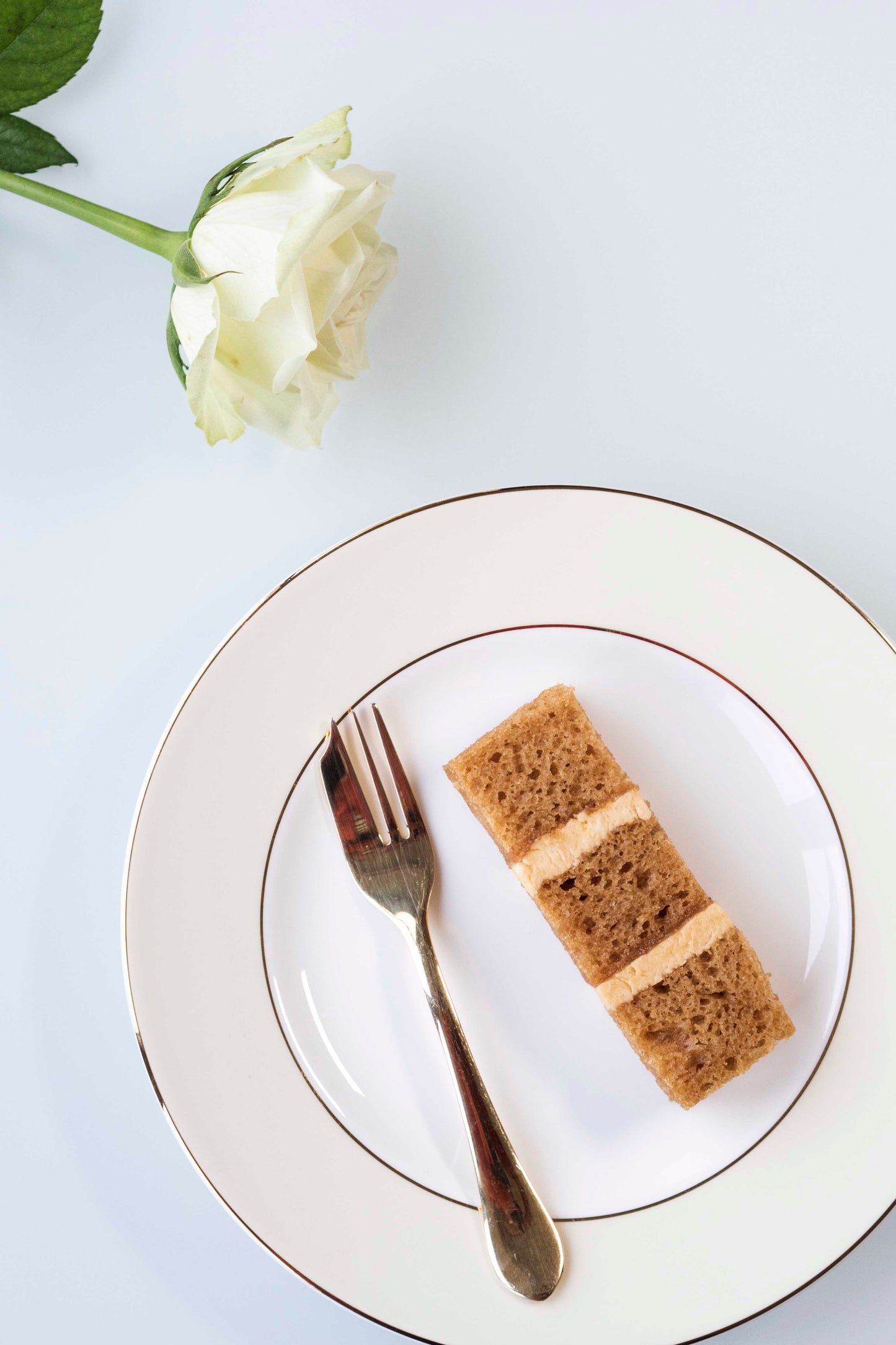 Single slice of toffee wedding cake with salted caramel buttercream on plate with gold fork and white rose