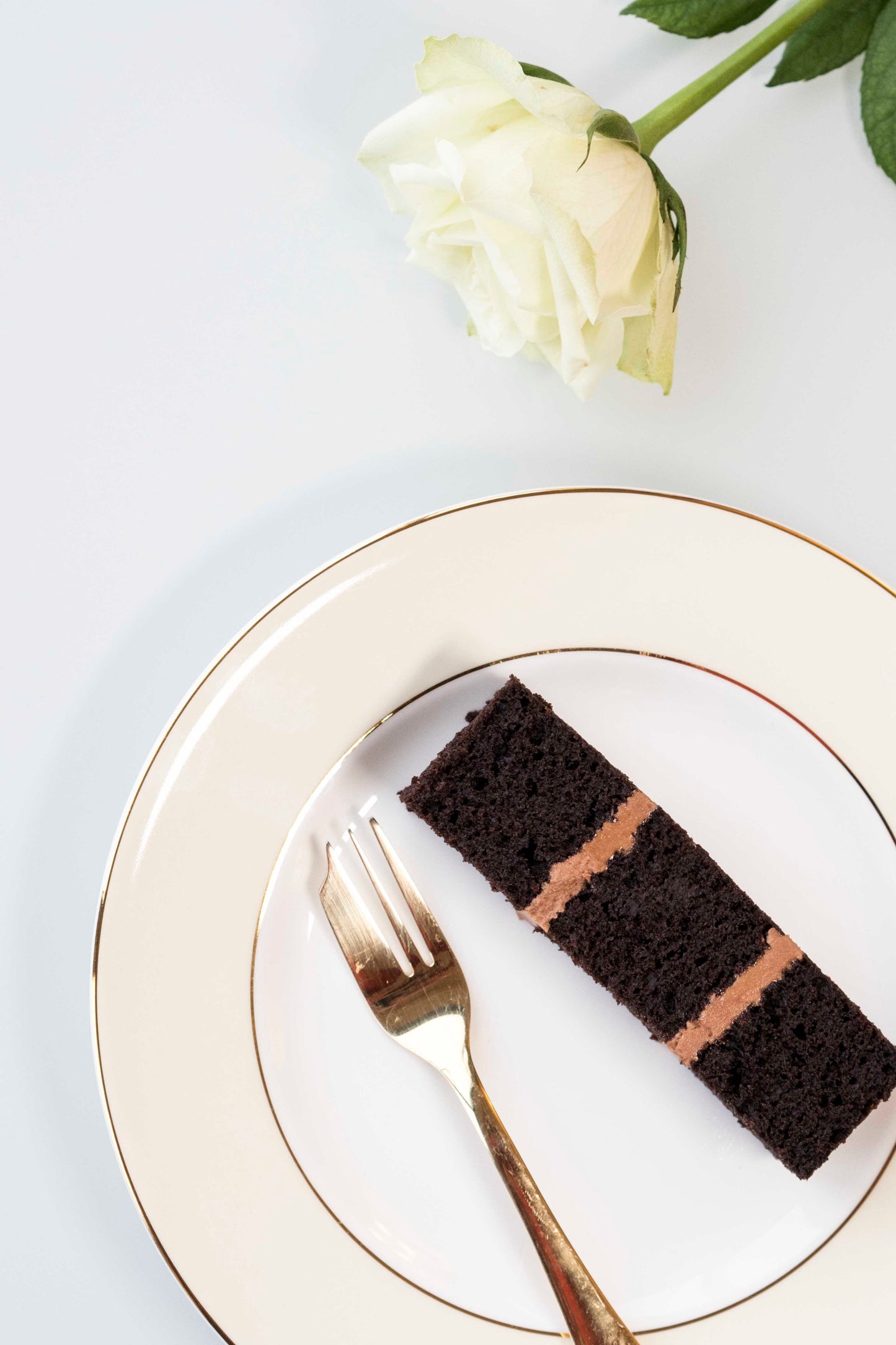 Single slice of chocolate wedding cake with chocolate buttercream with plate with gold fork and white rose