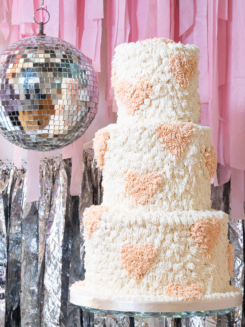 1970's inspired fringed wedding cake with peach hearts by the side of a glitter ball