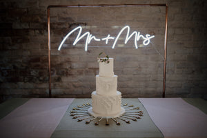 Macrame detail wedding cake in contemporary setting framed by "Mr and Mrs" neon lights