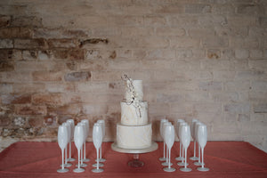 Modern wedding cake against whitewashed wall with white champagne glasses. Wedding cakes for Cheshire, Lancashire, Merseyside and Yorkshire
