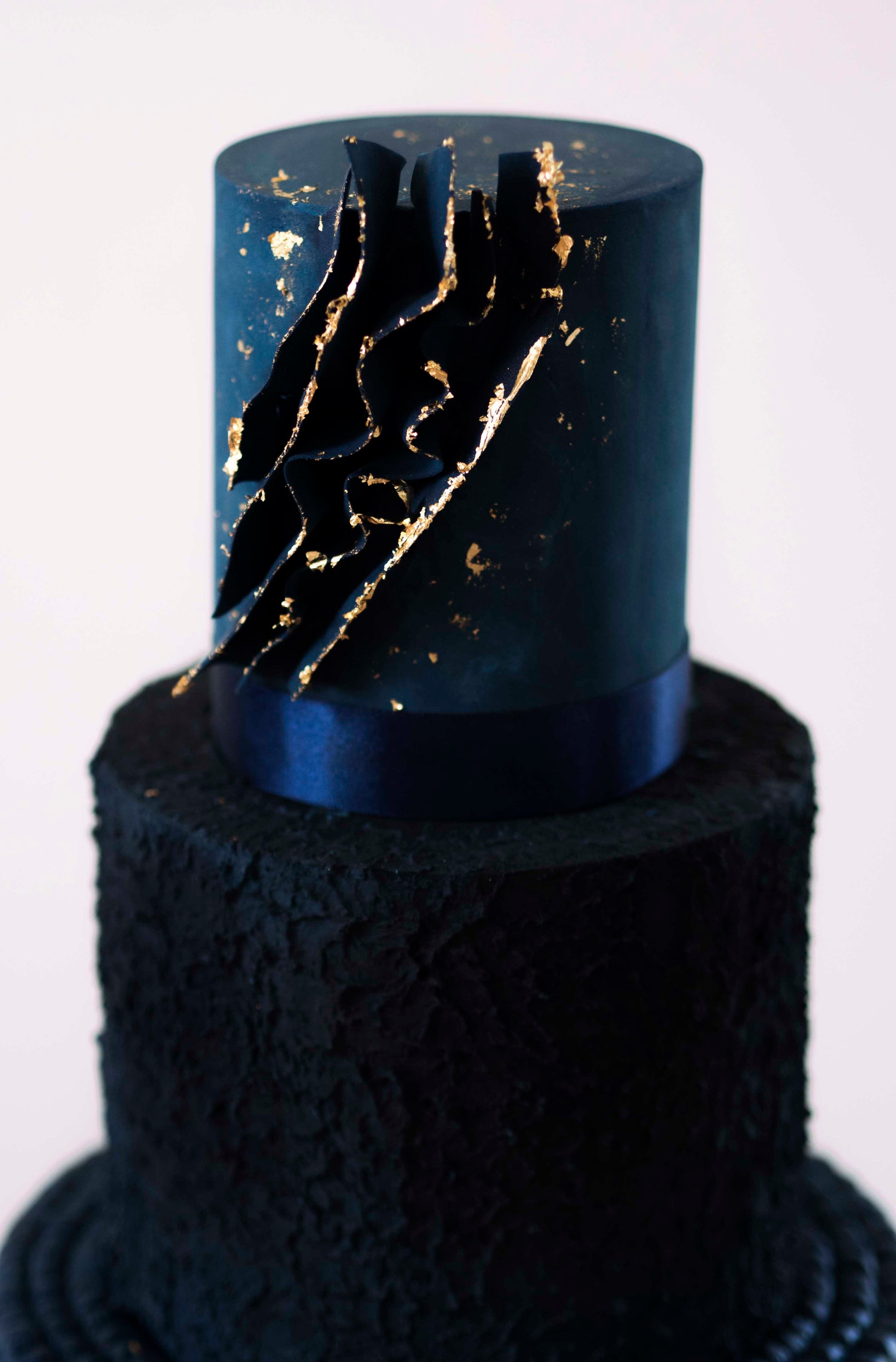 Edible blue sugar voile edged in royal gold leaf embellishes a three tier modern wedding cake in deep blue