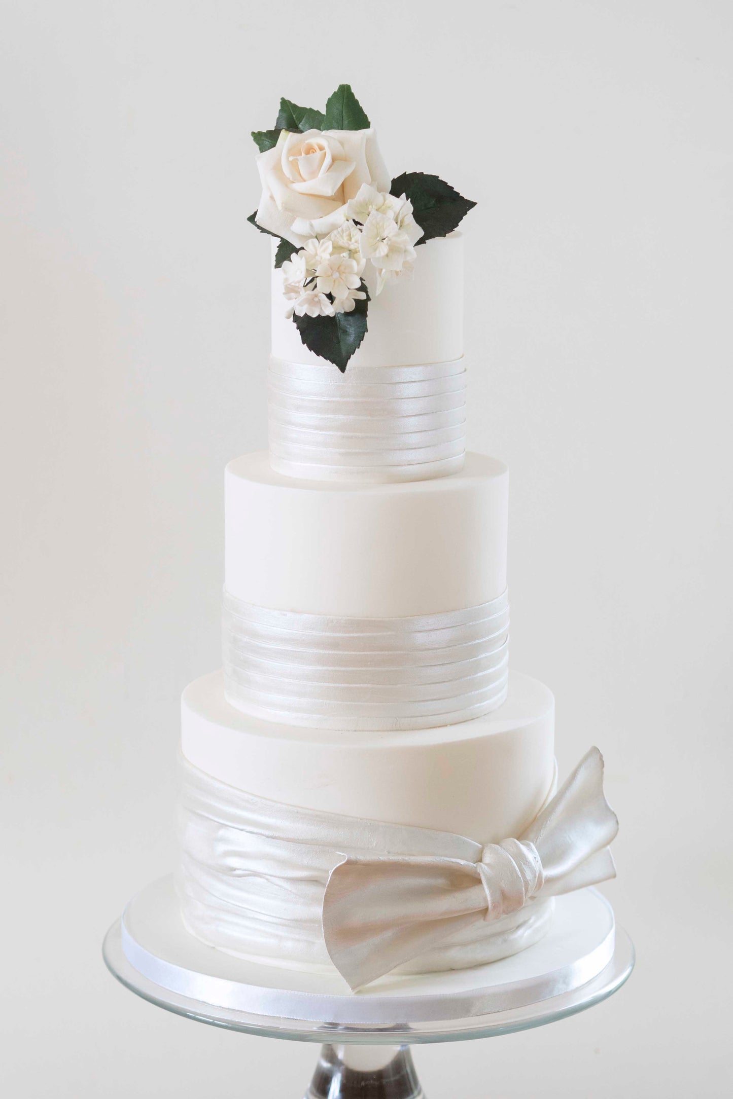 Three tier ivory wedding cake partially wrapped with pearlescent satin effect sugarpaste, topped with a white sugar rose