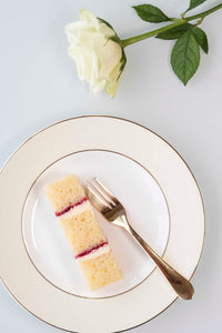 Single slice of vanilla sponge wedding cake with raspberry conserve on plate with gold fork and white rose