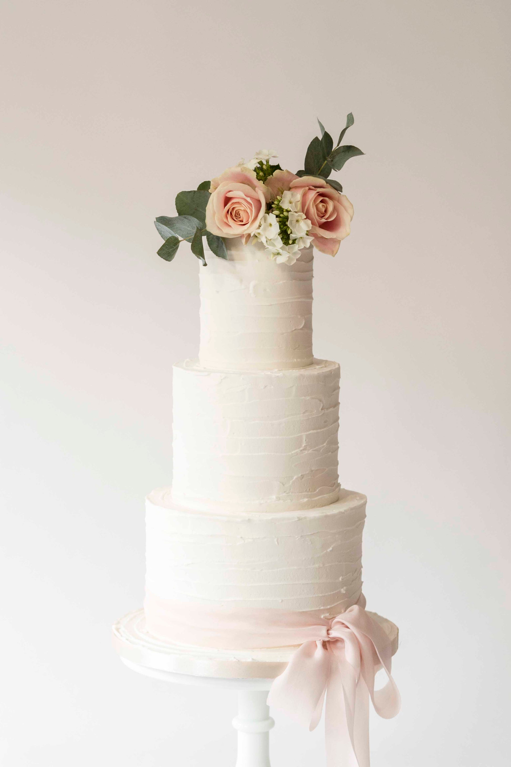 Buttercream effect textured wedding cake styled with fresh flowers and foliage and silk ribbon