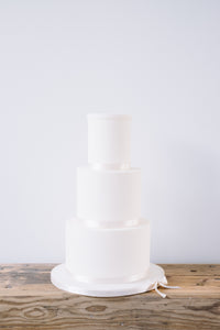 Our version of a naked wedding cake. Finished in smooth sugarpaste and neutral ribbon