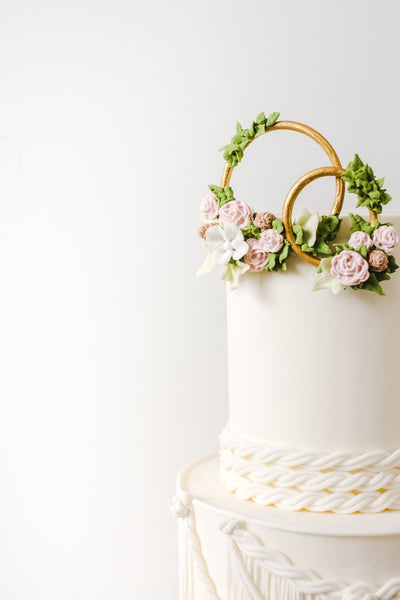 Gold rings decorated with sugar flowers on top of boho style wedding cake with sugar macrame lace