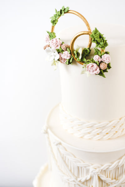Gold rings decorated with sugar flowers on top of boho style wedding cake with sugar macrame lace