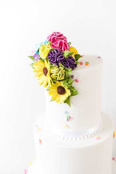 3 tier white wedding cake with contrasting colourful tassles on the base tier and matching ruffled top with sugar rudbekia. 