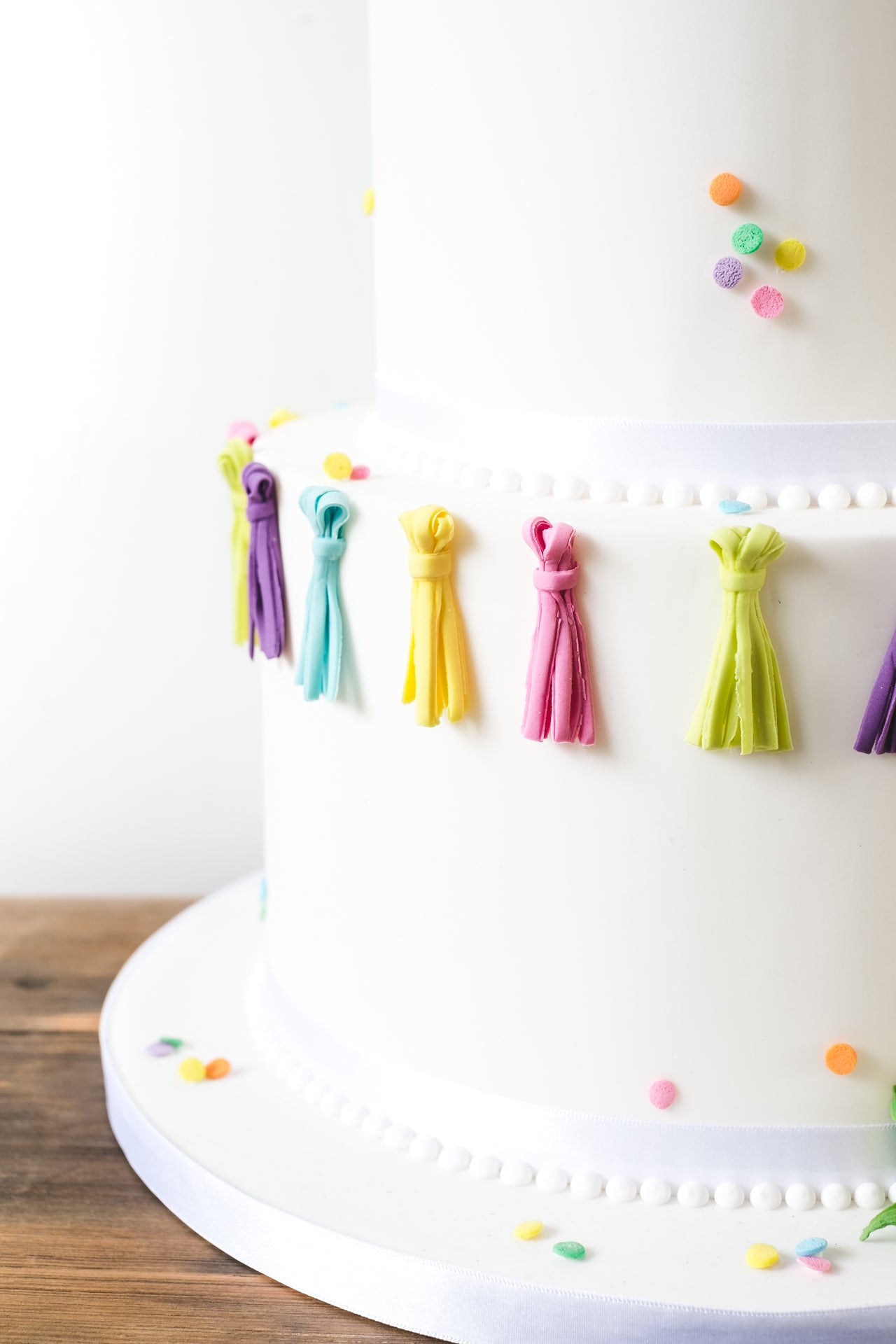 Fun, youthful, modern white wedding cake with pops of bright colour provided by tassles and colourful clusters.