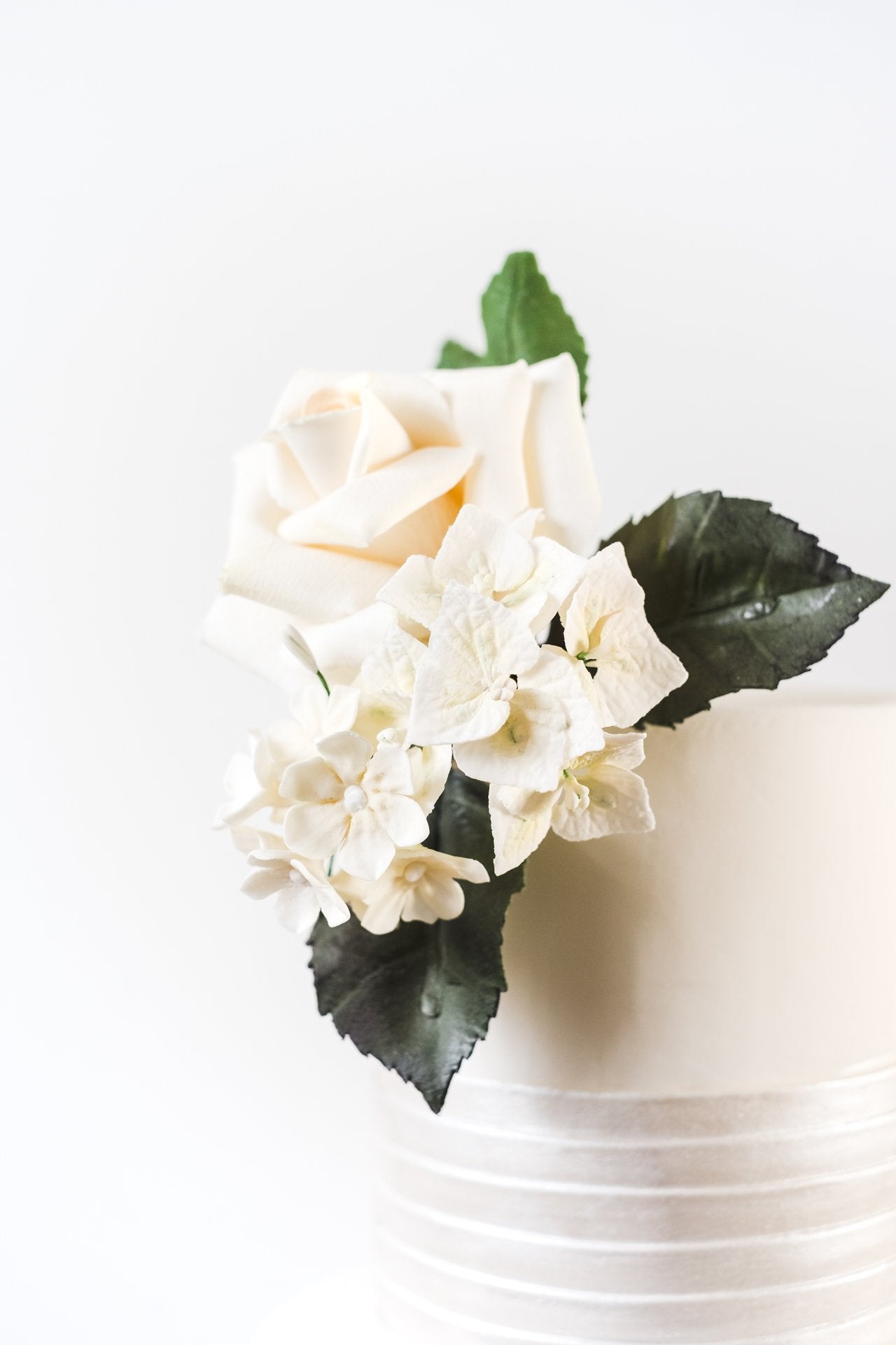 Top of contemporary ivory wedding cake with realistic white sugar rose, vivid green foliage and blossom flowers