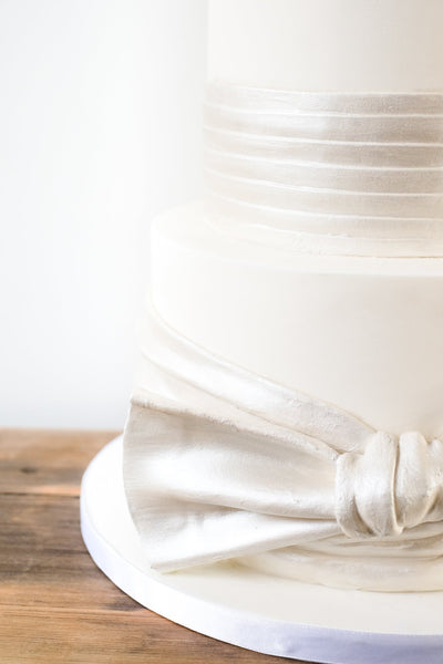 Oversized edible satin effect knot on a modern deep tiered ivory wedding cake with sharp edges