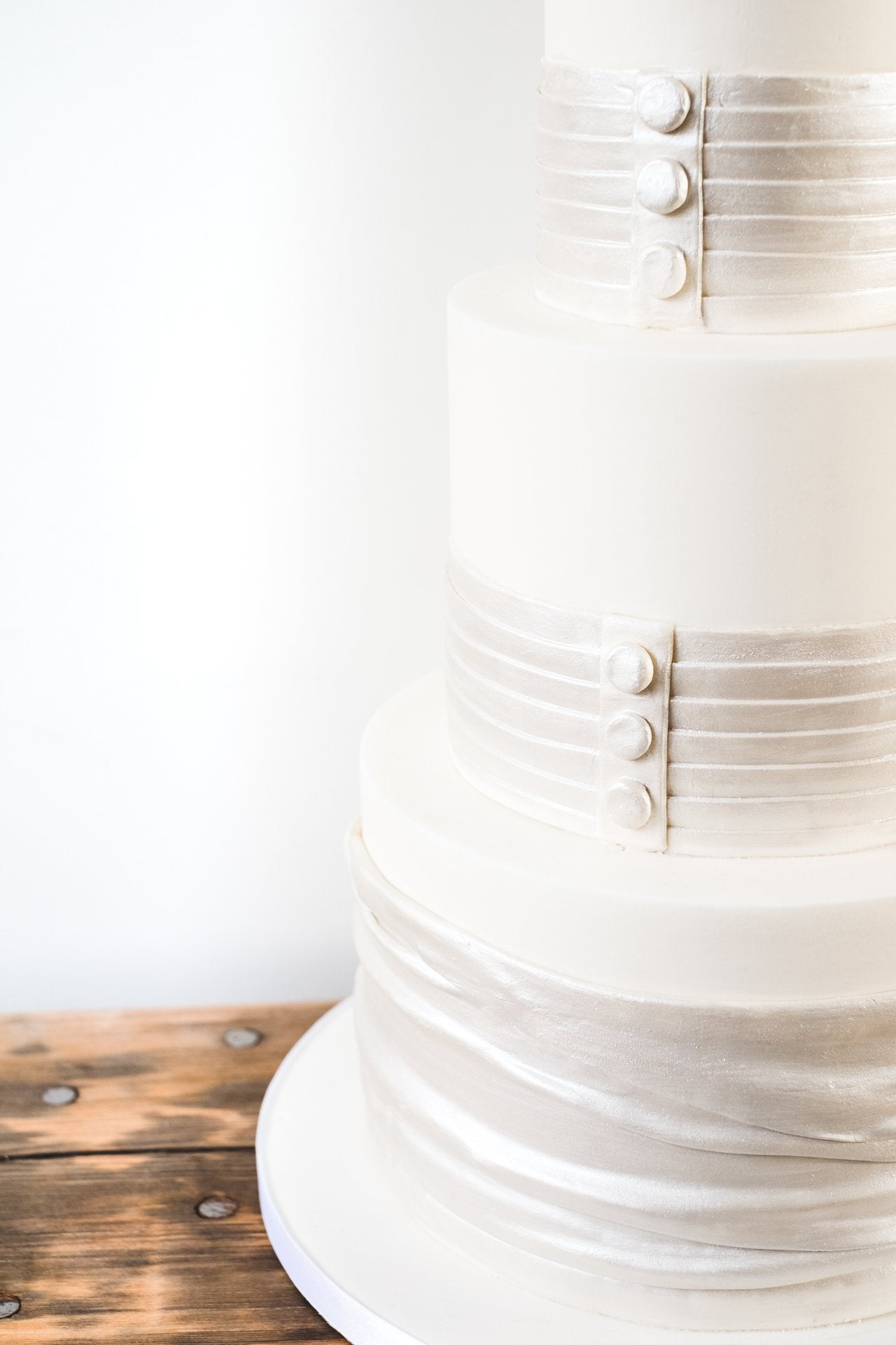 Deep tiered wedding cake decorated with bands of satin look sugarpaste with button detail like the back of a wedding dress.
