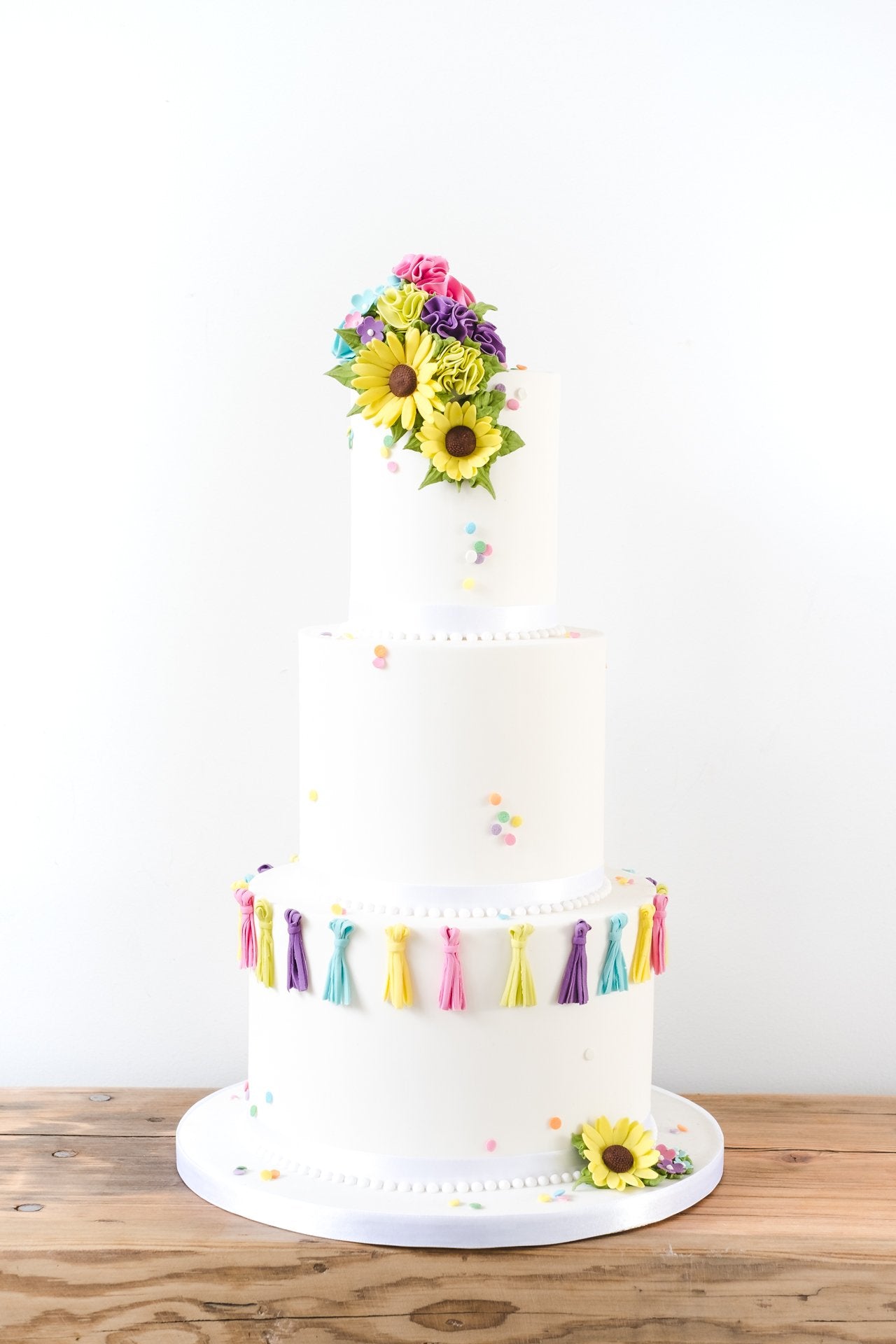 Contemporary white deep tiered wedding cake with pops of bright colour from sugar tassles and yellow sugar sunflowers by Saddleworth based Union Cakes