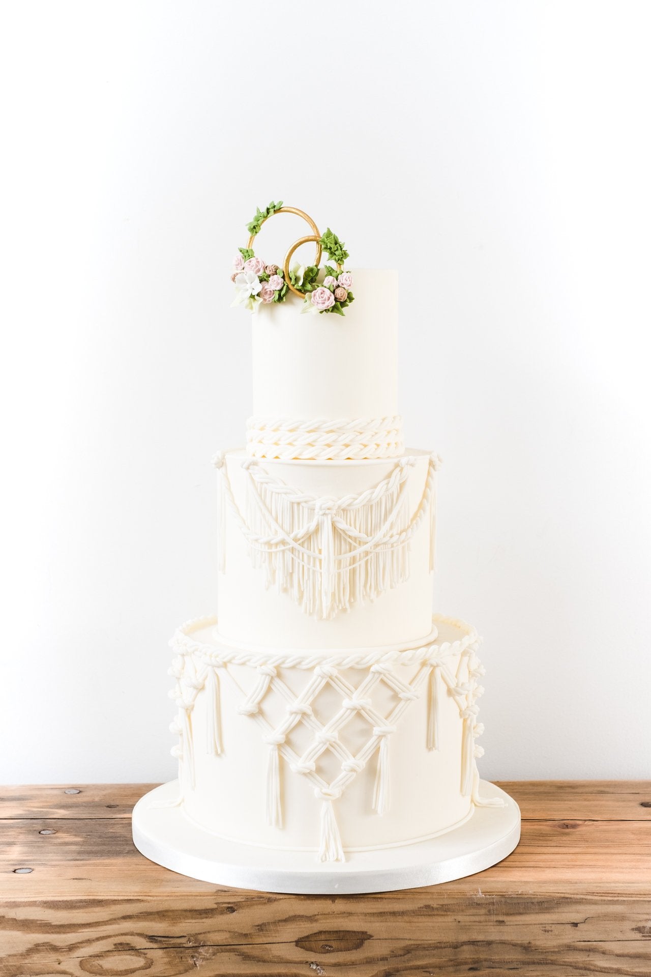 Three tier ivory boho wedding cake dressed with sugar macrame lace, topped with decorated gold rings